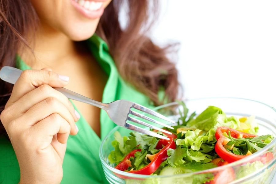 A beautiful woman eating fresh salad in order to prioritise health and avoid greasy fast food meal